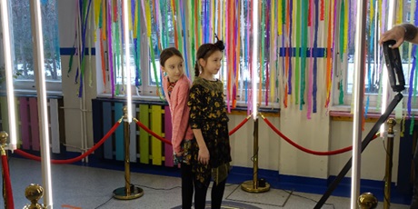 Powiększ grafikę: Dwie dziewczynki stoją na podeście oświetlonym lampami - patrzą w stronę kamery.