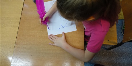 Powiększ grafikę: Dziewczynka pisze różowym ptasim piórem.