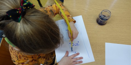 Powiększ grafikę: Dziewczynka rysuje żółtym ptasim piórem.