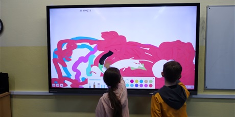 Powiększ grafikę: Dziewczynka i chłopiec rysują coś na multimedialnej tablicy.