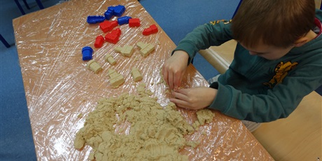 Powiększ grafikę: Chłopiec buduje coś z piasku. Na ławce leża różne foremki.