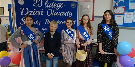 Powiększ grafikę: Grupa elegancko ubranych dzieci stoi przed tablicą z napisem 23 lutego dzień otwarty Szkoły Podstawowej nr 44 w Gdańsku.