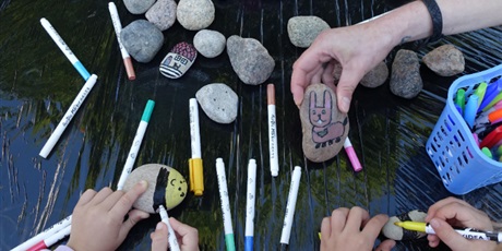 Powiększ grafikę: Dzieci tworzą obrazki kolorowymi mazakami na kamieniach.