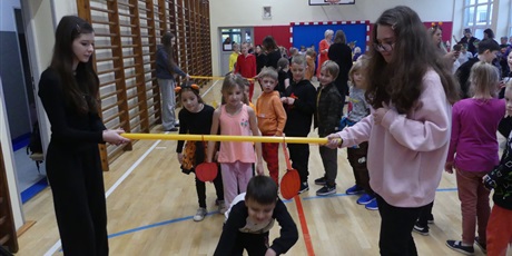 Powiększ grafikę: Dwie starsze dziewczyny trzymają plastikową rurkę, dzieci przechodzą pod nią.