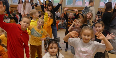 Powiększ grafikę: Grupa uśmiechniętych, przebranych na pomarańczowo dzieci, machają.