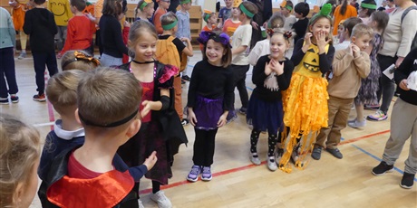 Powiększ grafikę: Grupa dzieci w różnych przebraniach - dziewczynka w stroju dyni, inna z opaską z uszkami. Stoją jeden obok drugiego, w coś się bawią.