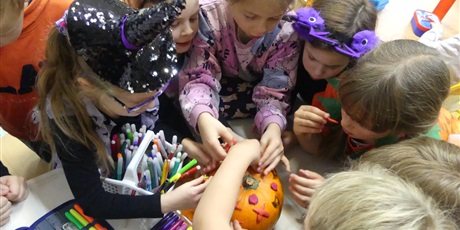 Powiększ grafikę: Grupa dziewczynek ozdabia dynię - przyklejają na nią ozdoby z plasteliny.