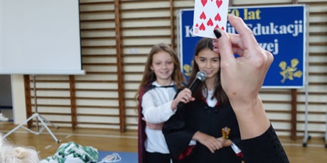 Powiększ grafikę: Ktoś w dłoni trzyma kartę do gry, w tle widać dwie dziewczynki.