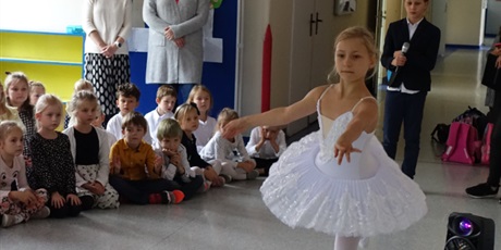 Powiększ grafikę: Dziewczynka ubrana w białą sukienkę tańczy przed innymi dziećmi.