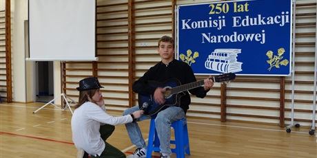 Powiększ grafikę: Chłopiec gra na gitarze, drugi trzyma mu mikrofon.
