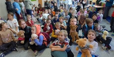 Powiększ grafikę: Grupa dzieci siedzi na podłodze, większość z nich trzyma w dłoniach pluszowe misie.