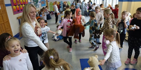 Powiększ grafikę: Dzieci tańczą w kółku z nauczycielką. Większość z nich trzyma w dłoni pluszowe misie. 