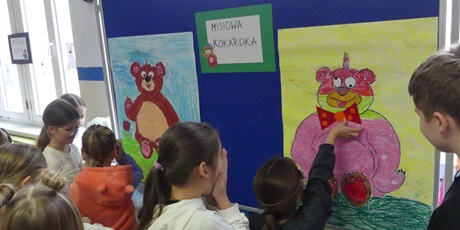 Powiększ grafikę: tablica z napisem misiowa kokardka i dwoma plakatami z misiami. Dzieci próbują z zamkniętymi oczyma przyczepić misiom kokardy.