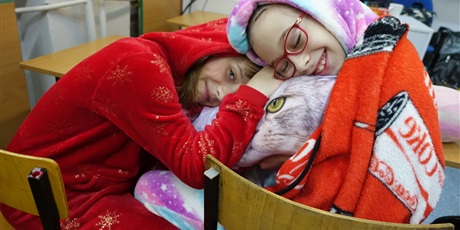 Powiększ grafikę: Dwie dziewczynki ubrane w kolorowe piżamy z kapturami ma głowach - leżą na poduszce.