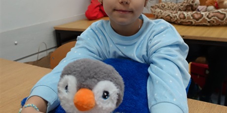 Powiększ grafikę: Dziewczynka w piżamie trzyma w dłoniach maskotkę pingwina.