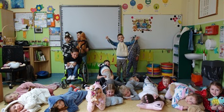 Powiększ grafikę: Grupa dzieci - ubrane w piżamy, mają w dłoniach poduszki i maskotki. Część z nich leży na podłodze.