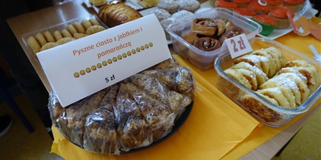 Powiększ grafikę: Stół ze słodkościami. Widać napis: Pyszne ciasto z jabłkiem i pomarańczą - 5 zł.