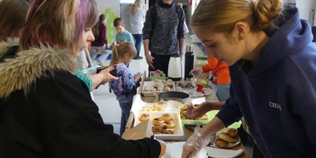Powiększ grafikę: Stoisko ze słodkościami - uczennica nakłada ciasto dziewczynce.