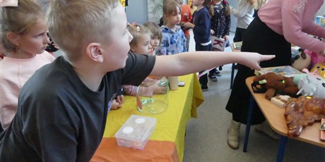 Powiększ grafikę: Grupa dzieci stoi przed stanowiskiem z loterią. Na pierwszym planie chłopiec, wskazuje na coś palcem wskazującym.