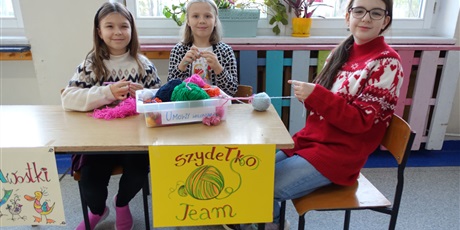 Powiększ grafikę: Trzy dziewczynki siedzą przy stole z napisem: Szydełko Team. W dłoniach mają szydełka i włóczki.