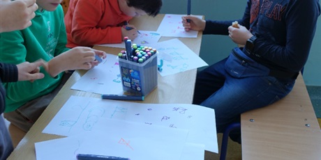 Powiększ grafikę: Chłopcy siedzą przy stole, rysują coś na kartkach. Widać napis: Zwierzaki z cyfr.