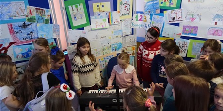 Powiększ grafikę: Grupa dzieci otacza dziewczynkę grającą na keyboardzie.