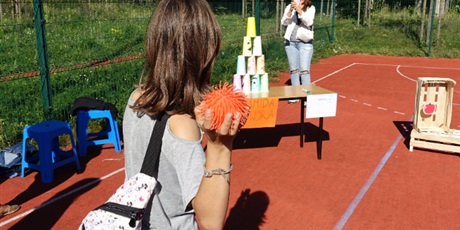 Powiększ grafikę: Uczennica rzuca pomarańczową piłką w wieżę ustawioną z papierowych kubków.