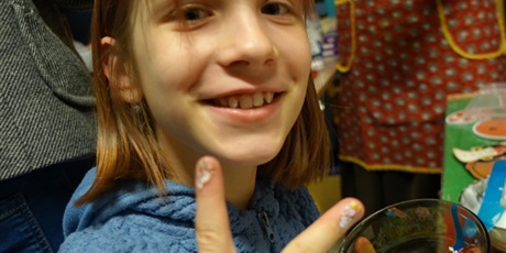 Powiększ grafikę: Uśmiechnięta dziewczynka pokazuje dwa palce, w dłoni trzyma miskę z kolorową posypką.