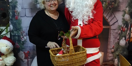 Powiększ grafikę: Uśmiechnięta pani dyrektor stoi z Mikołajem. Mikołaj trzyma w dłoni koszyk.