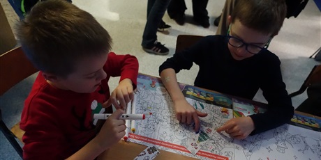 Powiększ grafikę: Dwóch chłopców siedzi przy stole, kolorują kolorowankę.