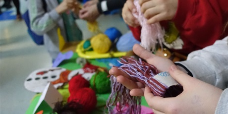 Powiększ grafikę: Dłonie dziecka trzymają kawałek tekturki owinięty kolorową włóczką.