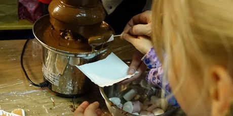 Powiększ grafikę: Czekoladowa fontanna - dziewczynka macza w niej piankę nabitą na wykałaczkę.