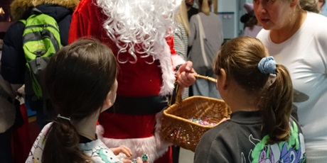 Powiększ grafikę: Święty Mikołaj stoi z koszem, przed nich dwójka dzieci.