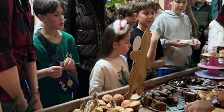 Powiększ grafikę: Stoisko z ciastami i słodkościami - przed nim stoi tłum dzieci i dorosłych, oglądają produkty.