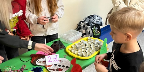 Powiększ grafikę: Chłopiec stoi przed stoiskiem, na którym robi się ozdobę świąteczną - zimowe czapeczki. 