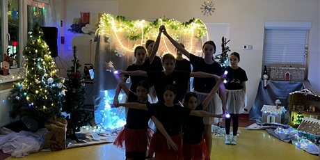 Powiększ grafikę: Dziewczynki wykonują układ taneczny - splatają ręce w taki sposób, że tworzą gwiazdę. W tle widać dekoracje świąteczne, zapalone światełka.