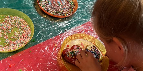 Powiększ grafikę: Dziewczynka dekoruje piernikowe serca. Na stole leżą talerzyki z kolorowymi posypkami.