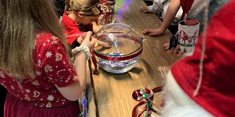 Powiększ grafikę: Dzieci przy stoisku, na którym leży szklana kula z losami.