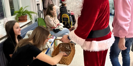 Powiększ grafikę: Święty Mikołaj częstuje siedzące na ławce dziewczyny cukierkami. 