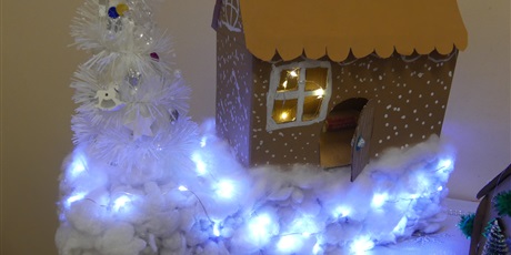 Powiększ grafikę: Praca plastyczna - domek wykonany z tektury. Przed domkiem śnieg z waty, ozdobiony światełkami.