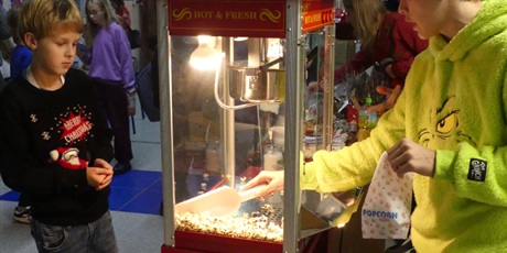 Powiększ grafikę: Budka z popcornem - chłopiec patrzy jak drugi chłopiec nakłada popcorn do papierowej torebki.