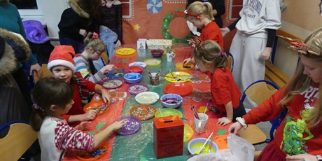 Powiększ grafikę: Stoisko kiermaszowe - dekorowanie pierników. Widać dzieci w trakcie dekorowania. Na stole leżą talerzyki z kolorowymi posypkami i lukrem.