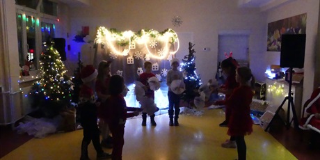 Powiększ grafikę: Grupa dzieci wykonuje taniec z parasolkami. Na sali jest ciemno, widać zapalone światełka, dekoracje świąteczne. 