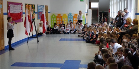 Powiększ grafikę: Dziewczynka stoi z mikrofonem przed grupą dzieci i nauczycieli.
