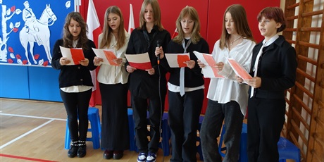 Powiększ grafikę: Grupa uczniów śpiewa, w dłoniach trzymają biało-czerwone kartki.