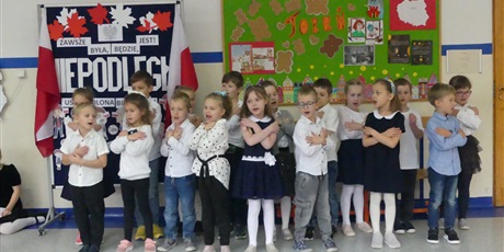 Powiększ grafikę: Grupa dzieci występuje na środku korytarza. Śpiewają piosenkę, pokazują jakieś gesty.