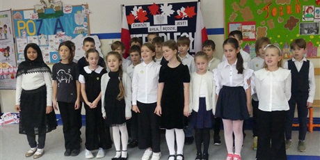 Powiększ grafikę: Grupa dzieci ubranych na galowo stoi na środku korytarza, występują.