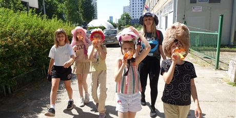 Powiększ grafikę: Grupa uśmiechniętych dzieci i pani - na głowach mają kolorowe kapelusze, część z nich dmucha w gwizdki.