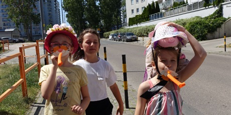 Powiększ grafikę: Trzy dziewczynki - dwie z nich mają kolorowe kapelusze na głowach, dmuchają w gwizdki.