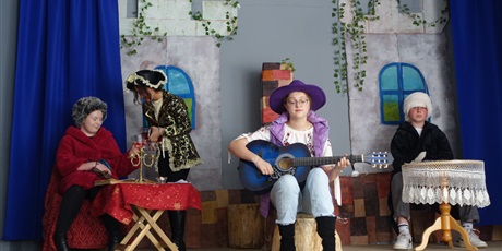 Powiększ grafikę: Na scenie widać czworo aktorów - ktoś nalewa napój do szklanki, ktoś gra na gitarze.